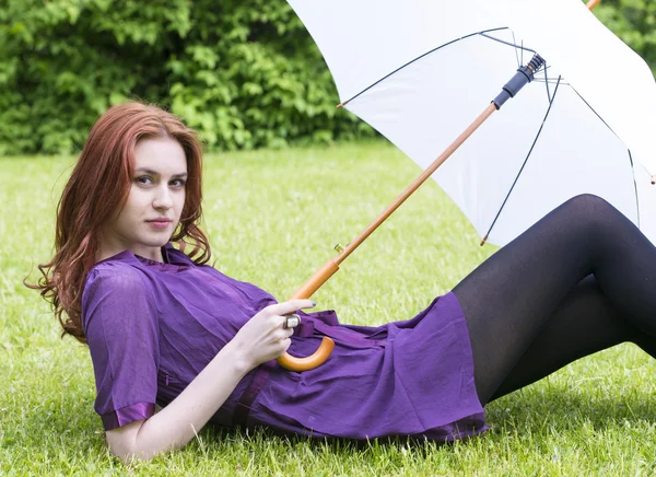 Jonge vrouw met paraplu ligt in een park — Stockfoto