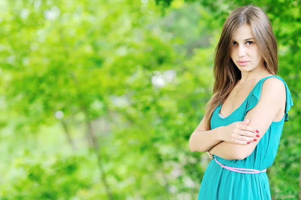 Beautiful woman outdoors with arms crossed against green backgro — Stock Photo, Image