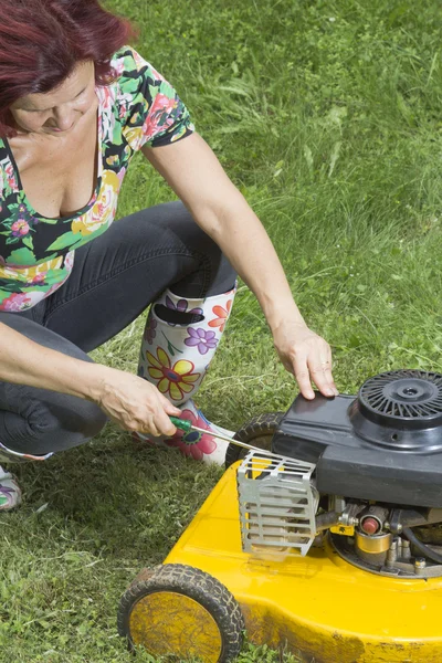 Woman repairs yellow lawn mower — Stock Photo, Image