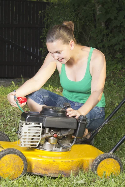 Милая девушка смазывает и ремонтирует желтую газонокосилку — стоковое фото