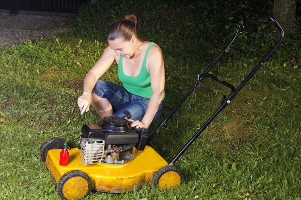 Cute girl repairing yellow lawn mower — Stock Photo, Image