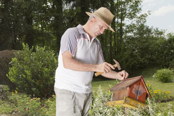 Усміхнений чоловік закріплює старий пташиний будинок — стокове фото