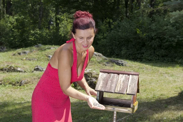 Женщина добавляет корм для птиц в птичий домик — стоковое фото