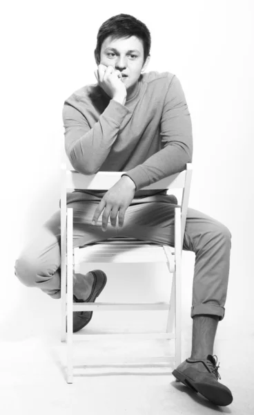 Ung vacker man sitter på en stol studio isolerade letar co — Stockfoto
