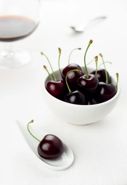 Cherries on white spoon and bowl, sherry glass on background — Stock Photo, Image