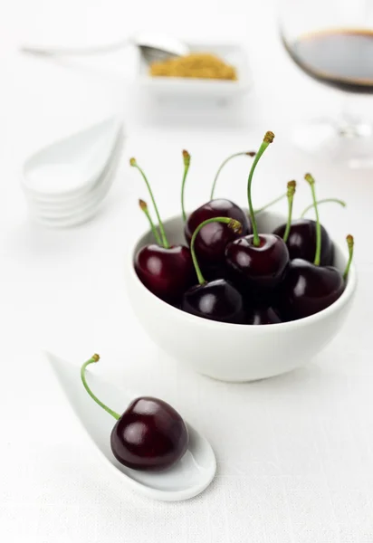 Cherries on white spoon and bowl, sherry glass, brown sugar — Stock Photo, Image