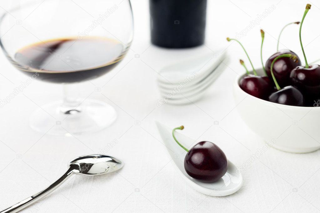 Cherries on white spoon and bowl, sherry glass, sugar cane