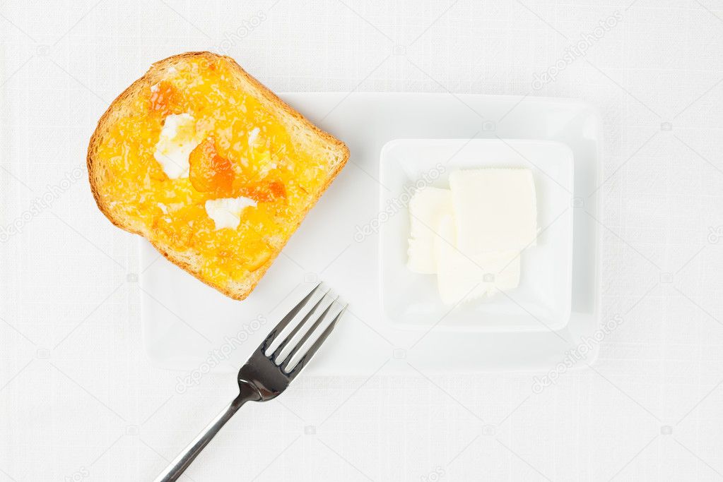 French toast, orange marmalade, butter, fork on white tablecloth