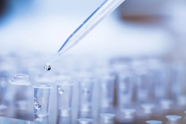 Pipette tip with droplet over rack of test tubes — Stock Photo, Image