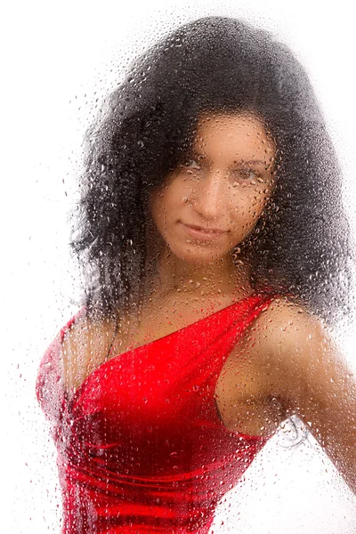 Menina bonita em um vestido vermelho, de pé atrás de um copo molhado em um fundo branco . — Fotografia de Stock