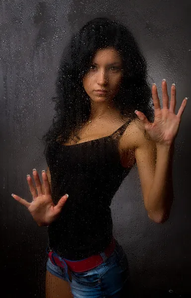Szép lány mögött sötét háttér előtt nedves üveg. — Stock Fotó