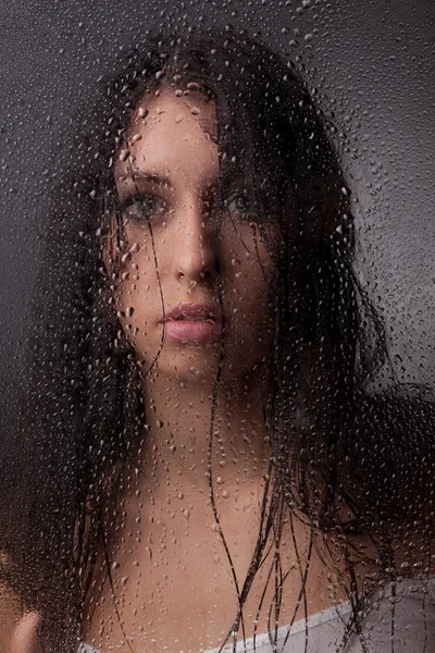 Een mooi meisje op een zwarte achtergrond achter het glas. Stockafbeelding