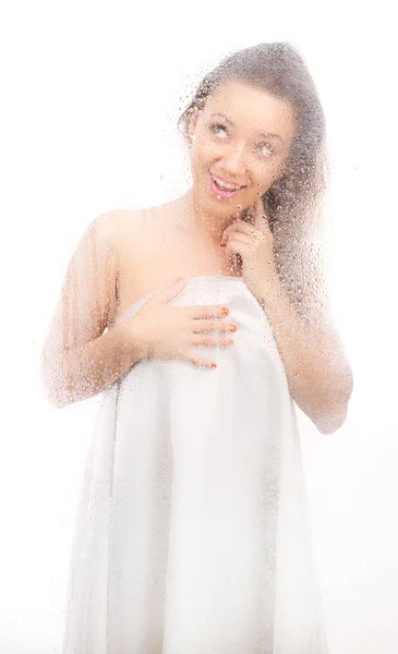 Mooi meisje in een wit vel achter een nat glas. — Stockfoto