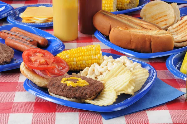 Um hambúrguer numa mesa de piquenique carregada de comida — Fotografia de Stock