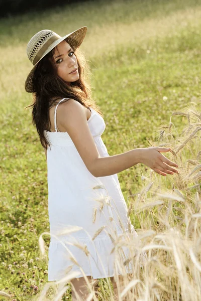 Молодая девушка в сенной шляпе трогает пшеницу в поле — стоковое фото