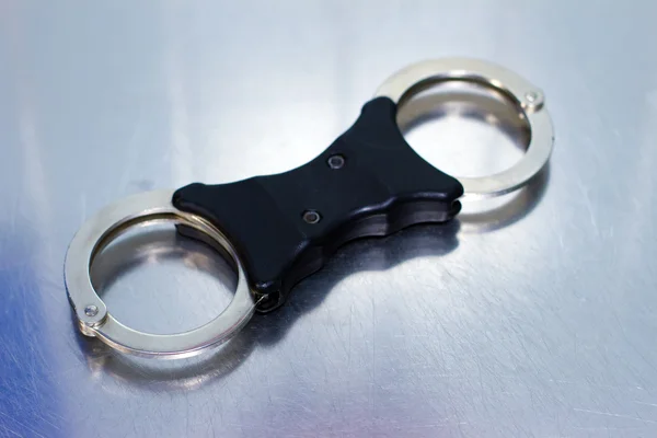 Handschellen im Polizeistil vor silbrig glänzendem Hintergrund — Stockfoto
