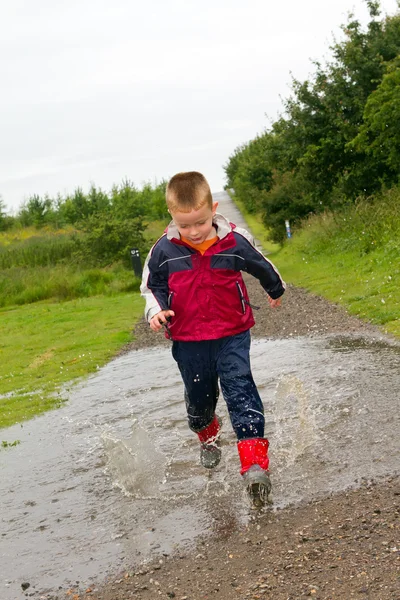 小男孩在一个水坑溅 — 图库照片
