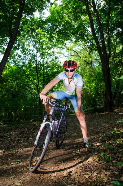Joven se para y sonríe en el bosque con la bicicleta — Foto de Stock