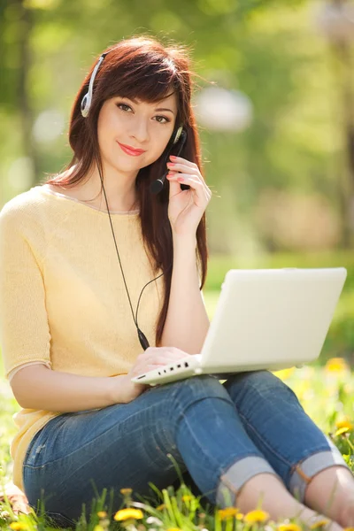 Kulaklık sevimli kadın parkta beyaz dizüstü bilgisayar ile — Stok fotoğraf