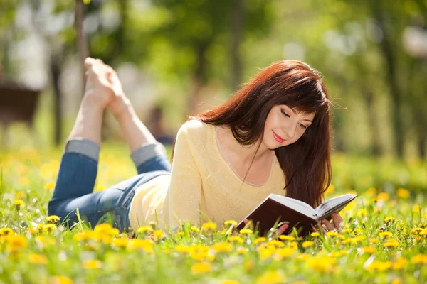 Młoda kobieta, czytanie książki w parku z kwiatami — Zdjęcie stockowe