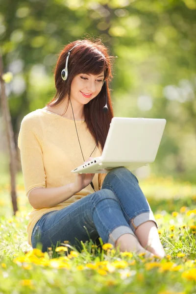 Mulher bonito em fones de ouvido com laptop branco no parque — Fotografia de Stock
