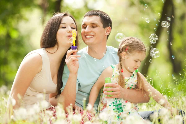 Mãe feliz, pai e filha soprando bolhas no parque — Fotografia de Stock