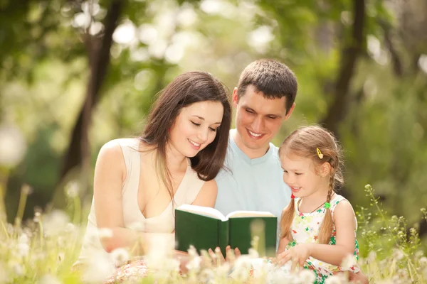 Madre, padre e figlia felici leggono un libro nel parco — Foto Stock