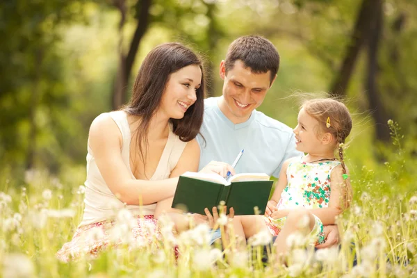 Glückliche Mutter, Vater und Tochter lesen im Park ein Buch — Stockfoto