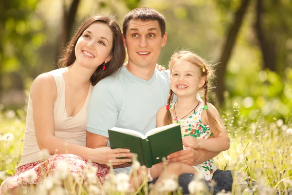Glückliche Mutter, Vater und Tochter lesen im Park ein Buch — Stockfoto