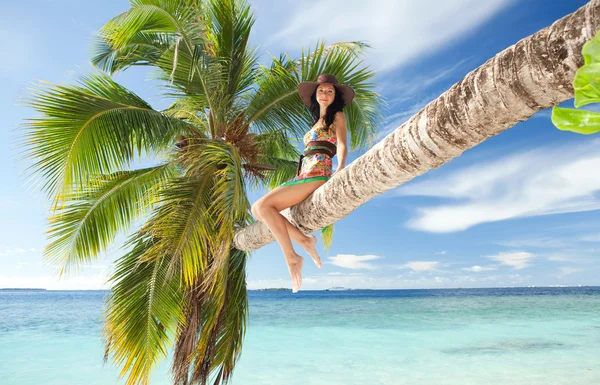Модна жінка сидить на пальмі на пляжі — стокове фото