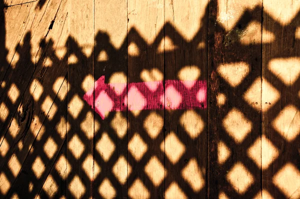 Розовая стрела с тенью забора на деревянном полу — стоковое фото