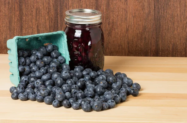 Blueberries spilling onto wooden table with jam