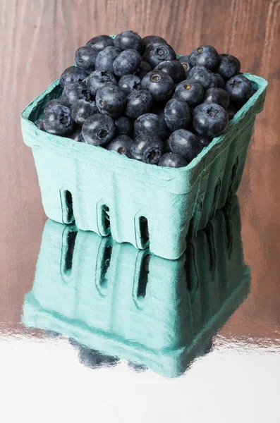 Green container of blueberries on shiny table — Stock Photo, Image