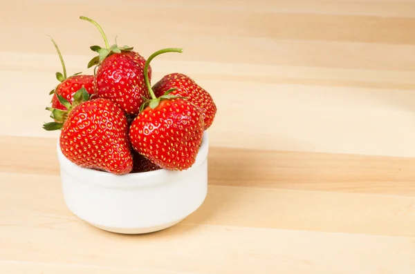 Aardbeien in witte kom op houten tafel — Stockfoto