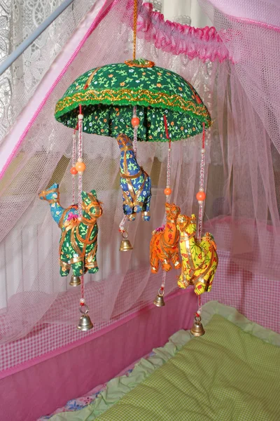 Brinquedos coloridos pendurados no berço com cortina de rede rosa vertical — Fotografia de Stock