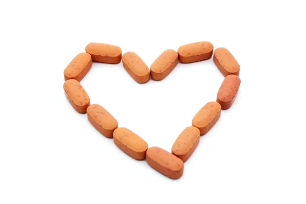 Comprimidos laranja em forma de coração isolado no fundo branco — Fotografia de Stock