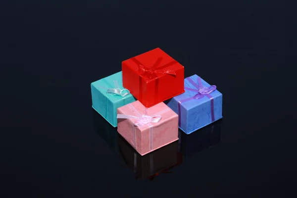 Τέσσερις πολύχρωμο δώρο κουτιά που απομονώνονται σε μαύρο φόντο με αντανάκλαση — Φωτογραφία Αρχείου