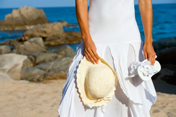 Mladá žena držící klobouk a flip flopy na pláži. — Stock fotografie