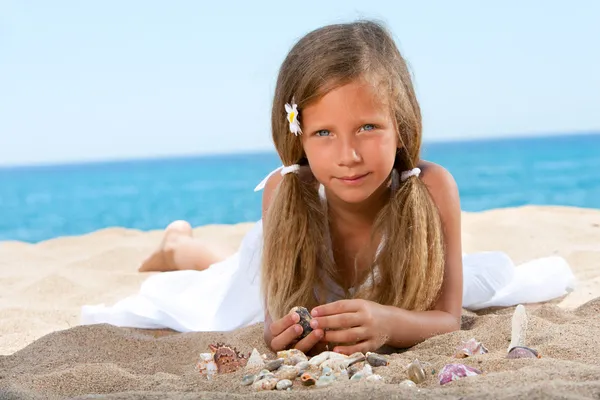 Милая девушка играет с раковинами на пляже . — стоковое фото