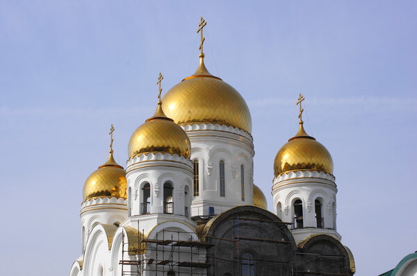 The upper part of the building of the Orthodox Church of the Nativity in the Siberian city of Krasnoyarsk (Russia). The golden domes of white walls in the background of gray-blue morning sky. Long shot. Summer, July of 2012.
