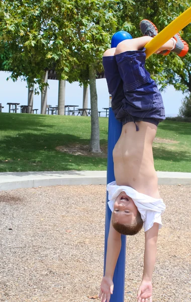 Хлопчик висить догори ногами в парку Стокове Фото