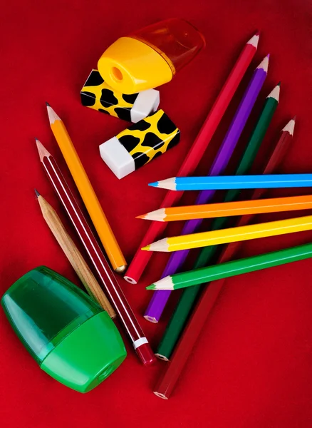 Gekleurde potloden, gummen, sharpeners geïsoleerd op rode achtergrond — Stockfoto