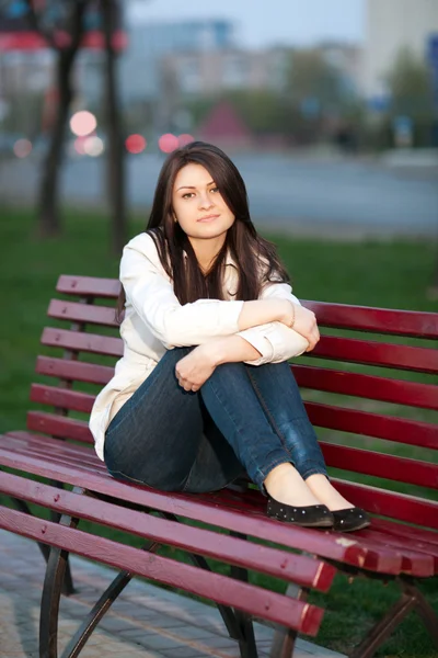 Chica en un parque de la ciudad en un banco — Foto de Stock