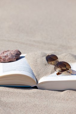 Sunglasses lies on an opened book on the beach clipart