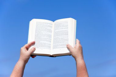 Woman's hands keep an open book in the blue sky clipart