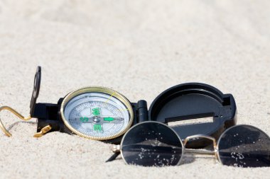 A compass and sunglasses lying on the hot desert sand clipart