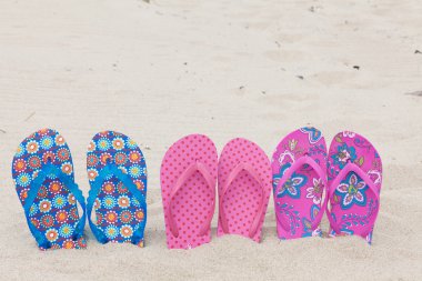 Three pairs bath slippers in a row stuck in the sand beach clipart