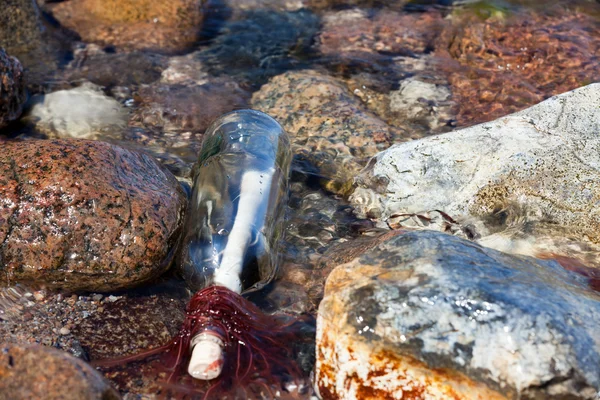Meddelande i en flaska i vattnet ligga på steniga stranden av Östersjön — Stockfoto