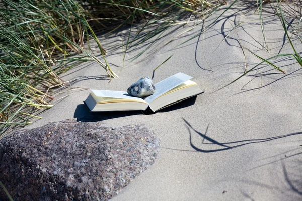 Leia na praia. Livro fica aberto na praia de areia entre a grama duna — Fotografia de Stock