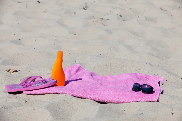 С шлепанцами, пляжным полотенцем, солнцезащитным кремом и солнцезащитными очками на пляже — стоковое фото